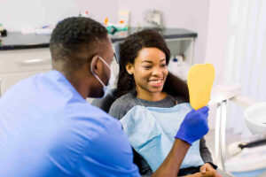 Male African dentist speaking with patient in dental clinic and shows her teeth in the mirror